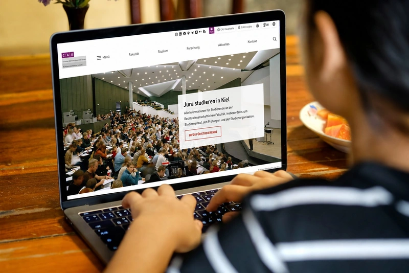 TYPO3-Multisite der Uni Kiel mit Fakultätswebsite Studierende nutzen den Webauftritt der Rechtswissenschaftlichen Fakultät der Uni Kiel auf einem Laptop.