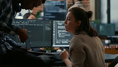 Zwei Entwickler arbeiten gemeinsam an Code und entwickeln individuelle Softwarelösungen in einer Open-Source-Umgebung