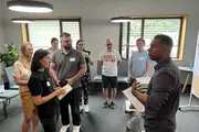 Jeury Tavares steht vor einer Gruppe von Pluswerk-Mitarbeitenden und leitet eine interaktive Übung an. Die Teilnehmenden hören aufmerksam zu und sind aktiv eingebunden.