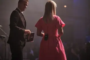 Die Moderatorin Emily Whigham steht im pinken Kleid auf der Bühne, neben ihr Matt Beadle mit einem Moderationskarten-Set. Beide richten sich an das Publikum der TYPO3 Award Gala 2025.