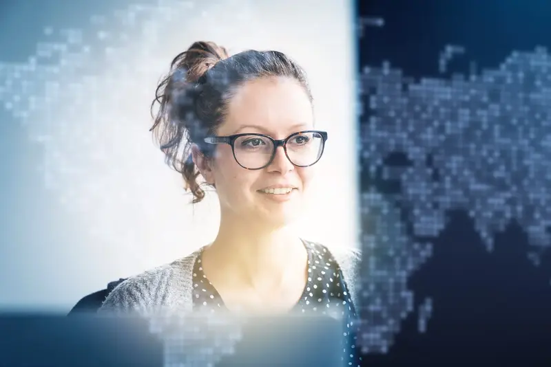 Eine Mitarbeiterin arbeitet konzentriert am Computer. Im Vordergrund sind digitale Daten- und Netzwerkgrafiken eingeblendet, die Analyse und Online-Marketing symbolisieren.