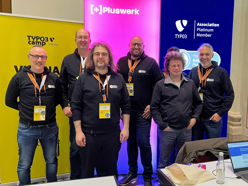 +Pluswerk Team am Stand des TYPO3Camp Vienna 2025 Gruppenfoto des +Pluswerk Teams vor dem Sponsorenstand beim TYPO3Camp Vienna 2025