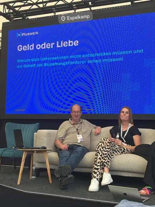 Jens Krumm (CEO +Pluswerk) und Janna Zapke (HR Mittwald) sitzen gemeinsam auf der Bühne während ihrer Session zu New Pay und Gehalt als Beziehungsfaktor.
