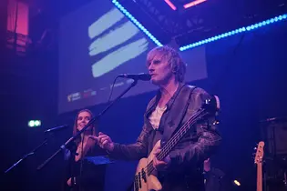 Ein Musiker der Tribute-Band „Reggatta de Blanc“ tritt auf der TYPO3 Award Gala 2025 auf. Er spielt Bass und singt, umgeben von violett-blauem Bühnenlicht.