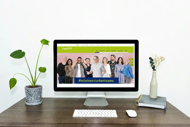 Laptop zeigt die neue ComTS Website mit dem Slogan „#teileinesstarkenteams“ und einer Gruppe von Mitarbeitenden