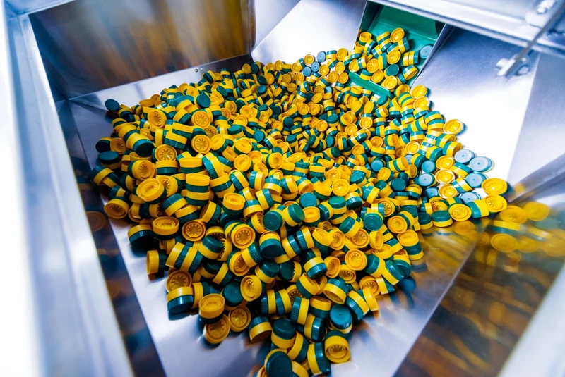 Große Menge gelb-grüner Kunststoffverschlüsse in einer industriellen Produktionsanlage für PET-Verpackungen, unsortiert in einem Metallbehälter.