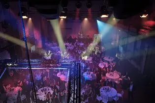 Blick von oben auf die TYPO3 Award Gala 2025: Rund eingedeckte Tische, Gäste in Abendkleidung und farbiges Bühnenlicht schaffen eine festliche Atmosphäre.