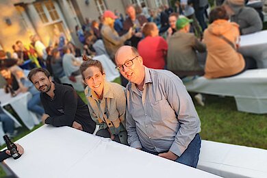 Bild des Gartens der Abendveranstaltung der TYPO3 University Days mit sitzenden Teilnehmern an weiß gedeckten Biertischen 