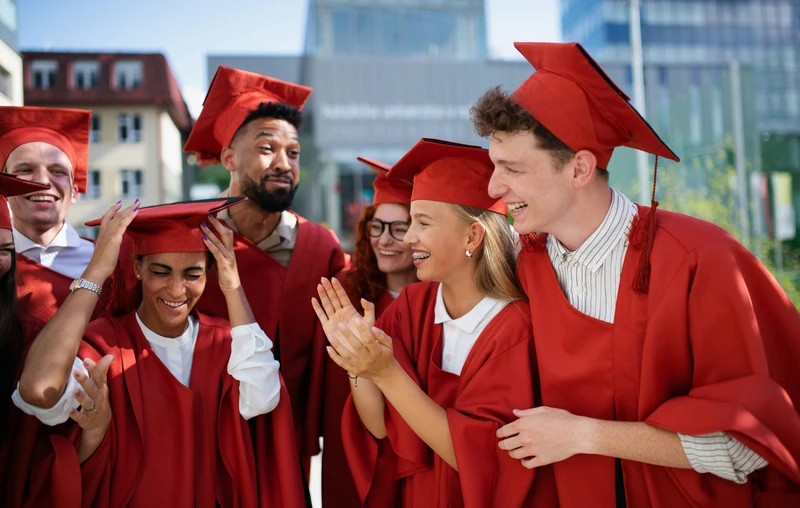 Comunicarea digitală în mediul universitar pentru studenții de astăzi și de mâine Un grup de absolvenți îmbrăcați în togi roșii și cu bonete de absolvire își sărbătoresc împreună absolvirea într-un campus universitar.