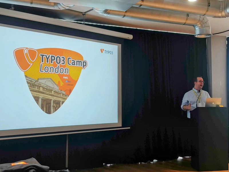Vortrag beim TYPO3 Camp London im MSQ Covent Garden Sprecher steht vor einer Leinwand mit dem Logo des TYPO3 Camp London und hält eine Präsentation im Veranstaltungsraum in Covent Garden.