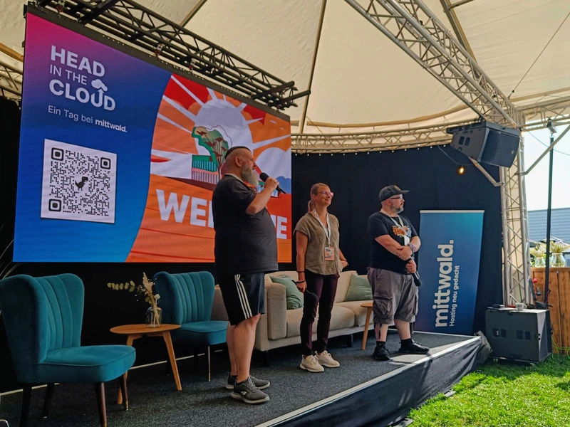 Drei Personen stehen auf der Open-Air-Bühne in Espelkamp: links Mittwald Geschäftsführer Florian Jürgens, in der Mitte Janna Zapke (HR Mittwald) und rechts Martin Helmich (Head of Developer Relations).