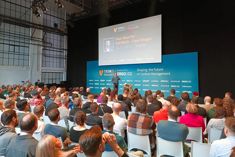 T3CON25 Core Stage with host Jeury Tavares Eine große Gruppe von T3CON25-Teilnehmenden sitzt im Core-Stage-Bereich des Areal Böhler und folgt der Begrüßung durch Host Jeury „Jerry“ Tavares. Auf der Bühne ist eine große Leinwand mit seinem Namen und Foto zu sehen.