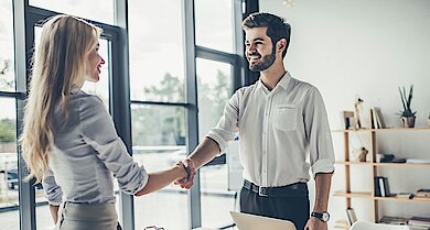 Geschäftlicher Handschlag zwischen Bewerberin und Arbeitgeber in moderner Büroumgebung.