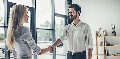 Geschäftlicher Handschlag zwischen Bewerberin und Arbeitgeber in moderner Büroumgebung.