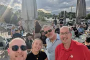 Gruppenfoto bei Sonnenschein auf einer Dachterrasse. Vier Personen blicken in die Kamera, im Hintergrund viele Menschen und Sonnenschirme. Von links nach rechts: Daniel Fau, Luisa Faßbender, Hans-Georg Raphael und Jens Krumm.