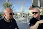 Zwei Männer sitzen bei Sonnenschein auf einer Terrasse mit Sonnenschirmen und unterhalten sich. Beide tragen Sonnenbrillen. Links: Georg Tiefenbrunn von Earlybird, rechts: Daniel Fau von der TYPO3 GmbH.