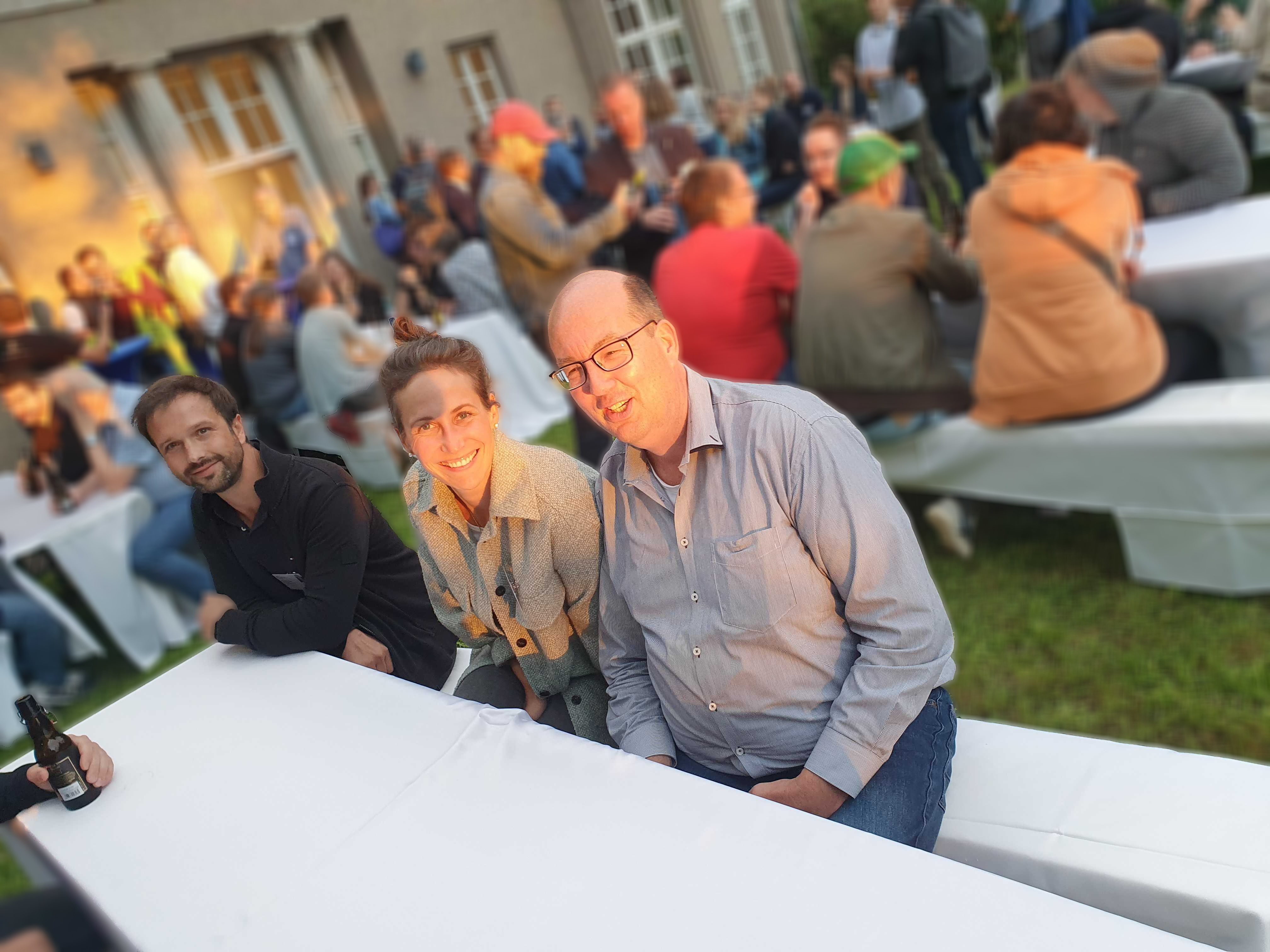 Bild des Gartens der Abendveranstaltung der TYPO3 University Days mit sitzenden Teilnehmern an weiß gedeckten Biertischen